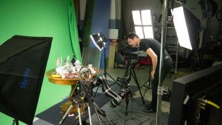 Ein Mann in einem Filmstudio filmt mit einer Kamera einen Kaffeehaustisch vor einer grnen Leinwand